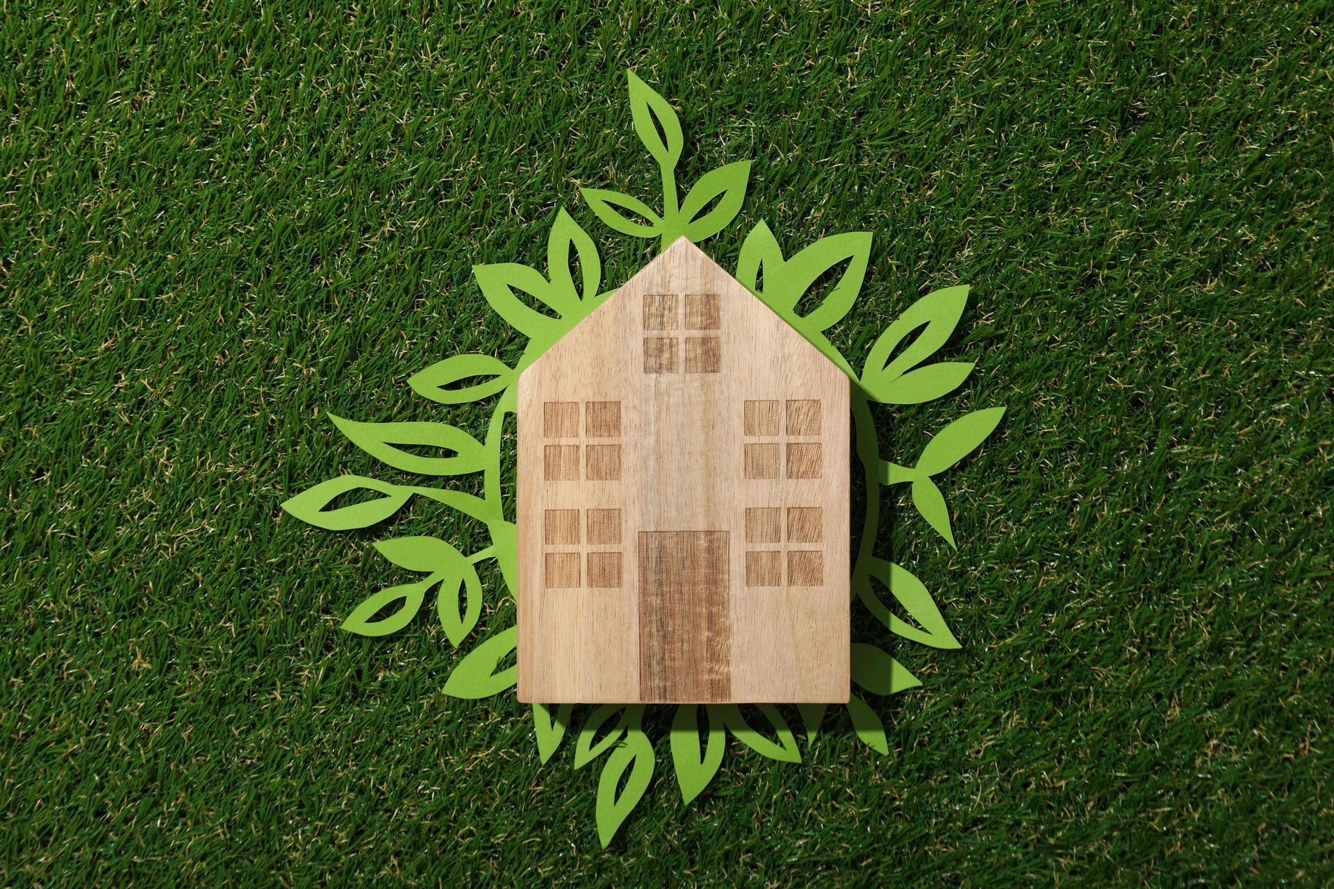 Eco‑themed house cutout on green grass framed by paper leaves.