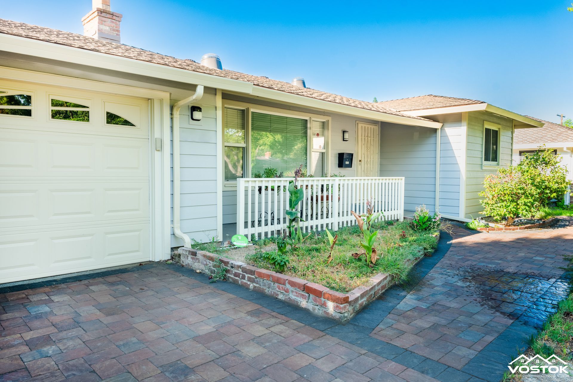 A white house with a brick driveway and a white garage door.