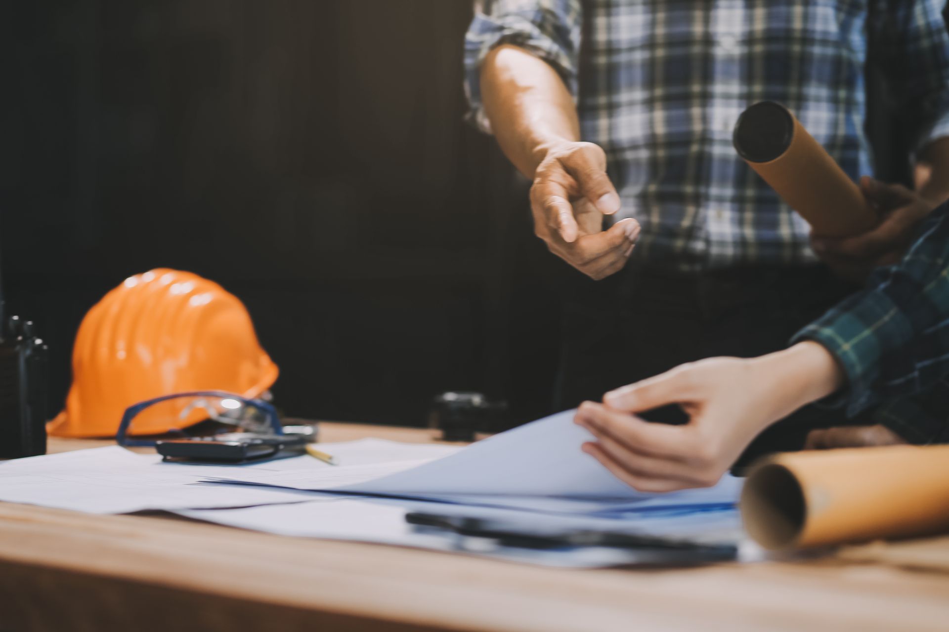 Two people reviewing construction plans at a table with safety gear and tools.