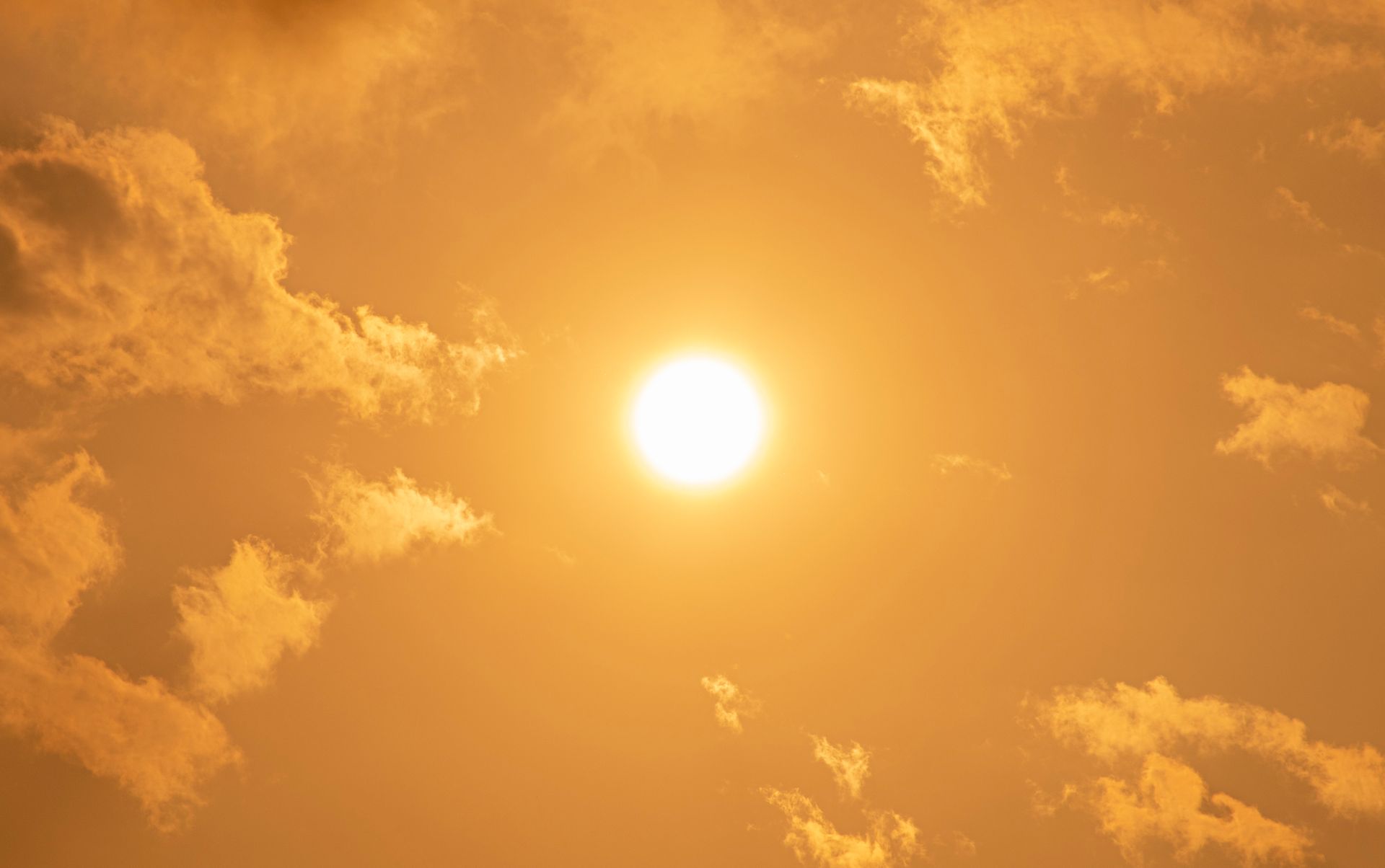 The sun is high in the sky surrounded by white clouds