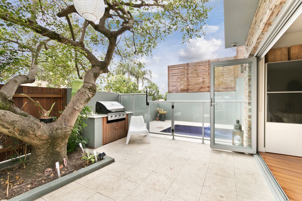 A Paved Outdoor Patio With A BBQ, A Tree, And A Glass-Fenced Pool — South East Kitchens In Burleigh Heads, QLD
