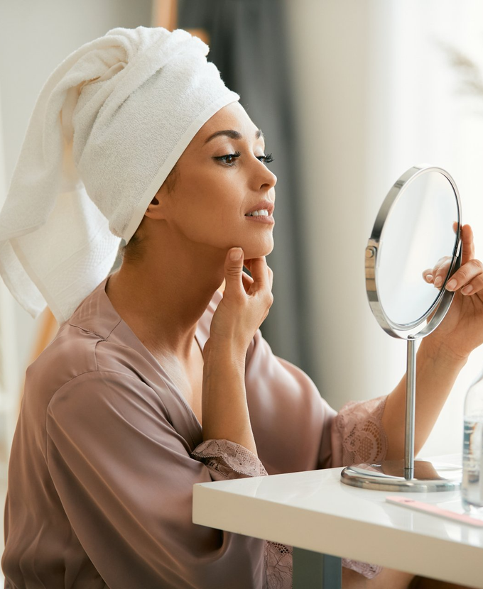 a woman looking at her double chin in a makeup mirror