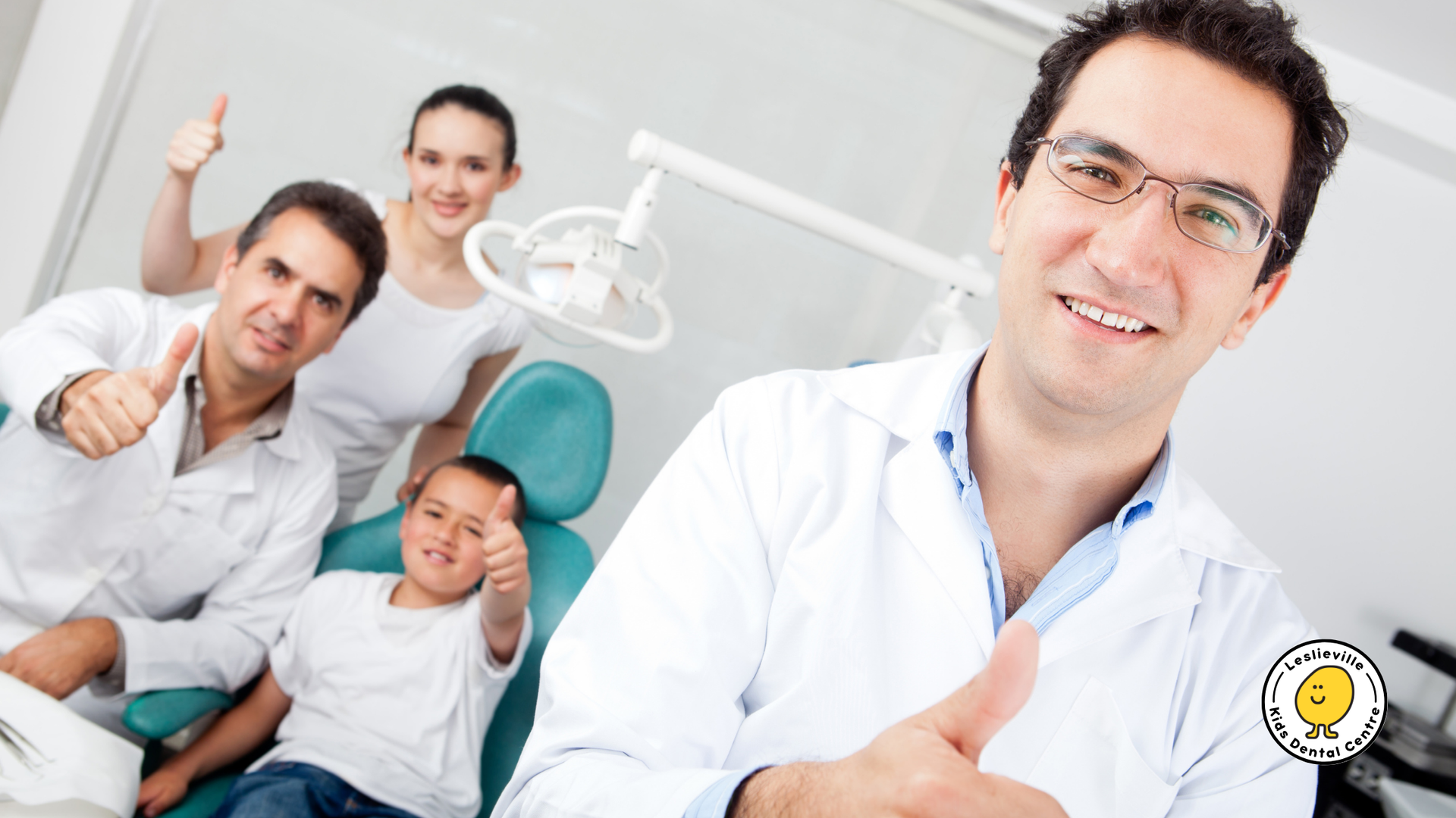 Dentists and family in a dental office give thumbs up, a child in a chair.
