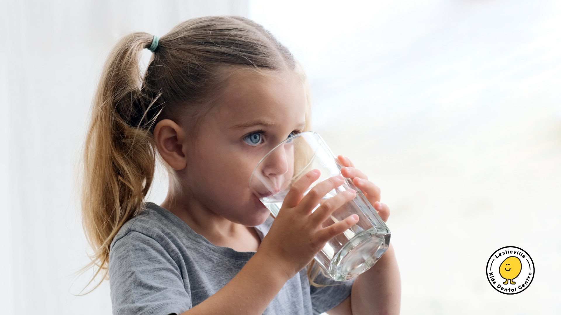 A little girl is drinking a glass of water.