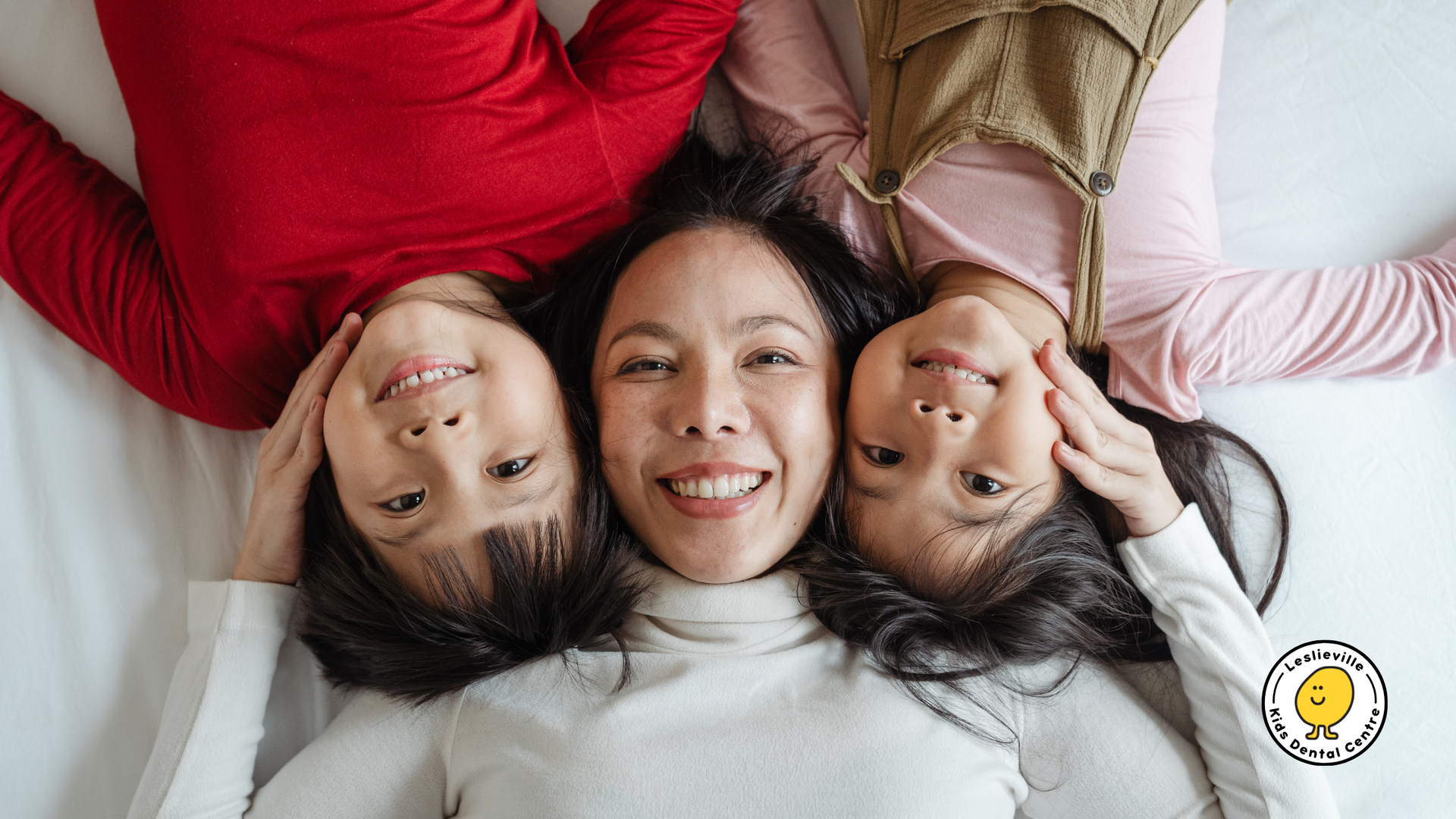 A woman and two children are laying on a bed with their heads together.