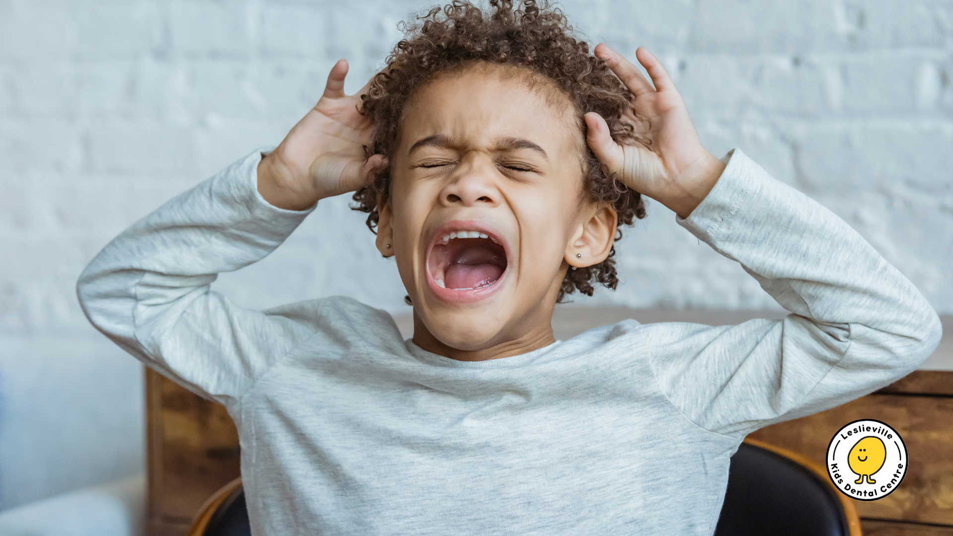 A young boy is sitting in a chair with his mouth open and holding his head.