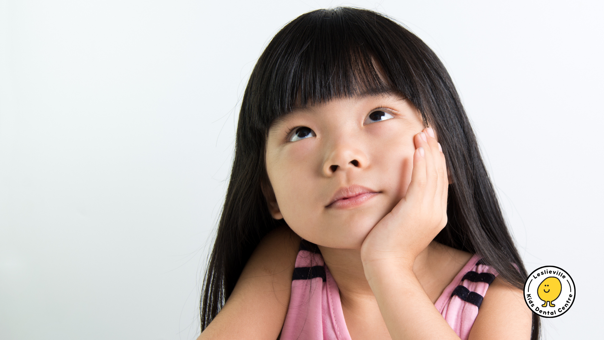 Girl with long black hair, pink top, looking up, resting chin on hand.