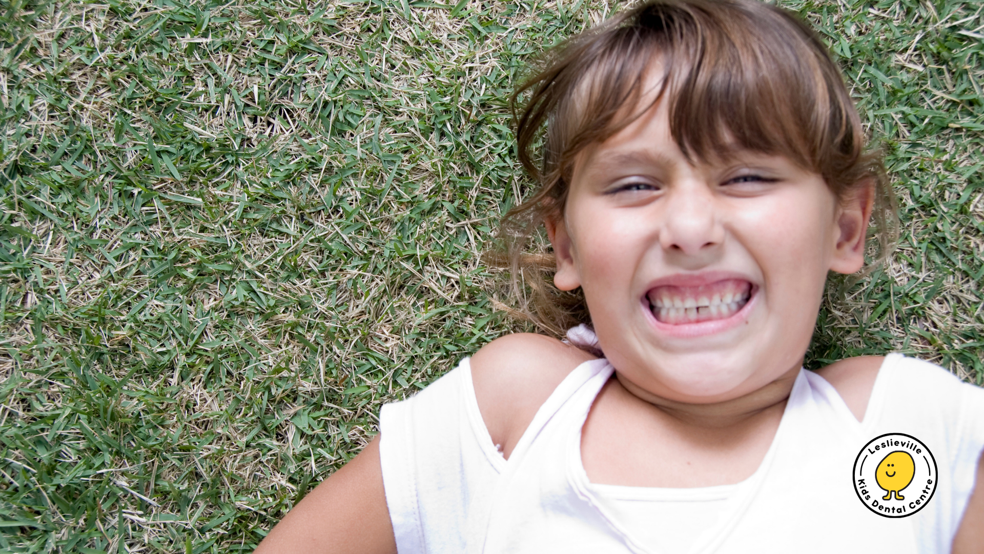 A little girl is laying on the grass with her mouth open