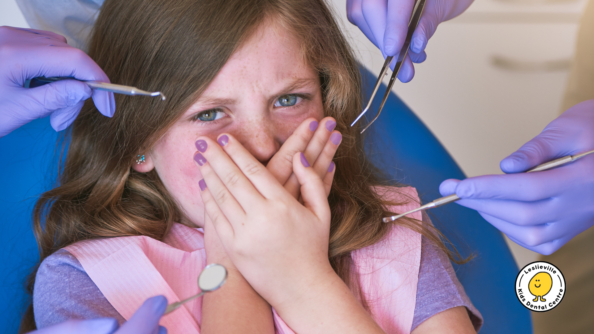 A little girl is sitting in a dental chair covering her face with her hands.