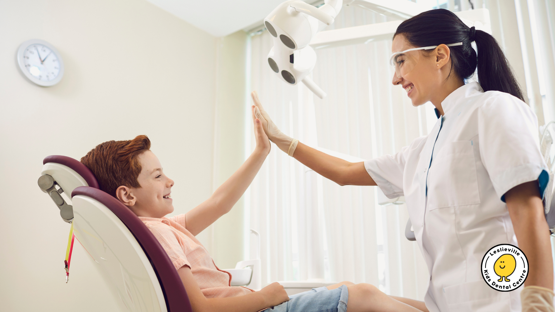 A dentist and a smiling boy in a dental chair give each other a high five. Light-filled room.
