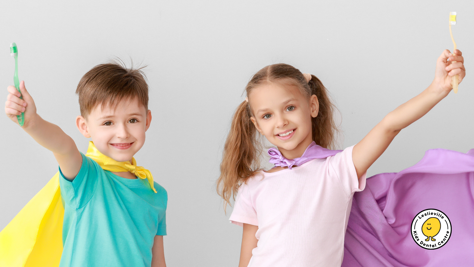 A boy and a girl are wearing capes and holding toothbrushes.
