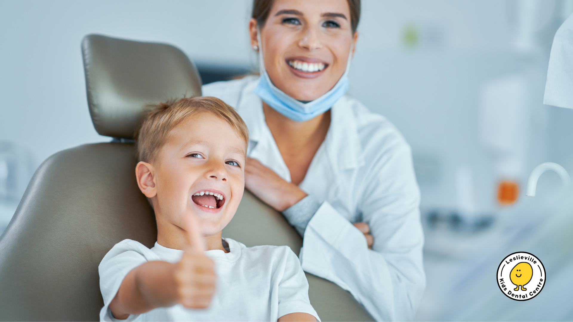 A young boy is sitting in a dental chair and giving a thumbs up.