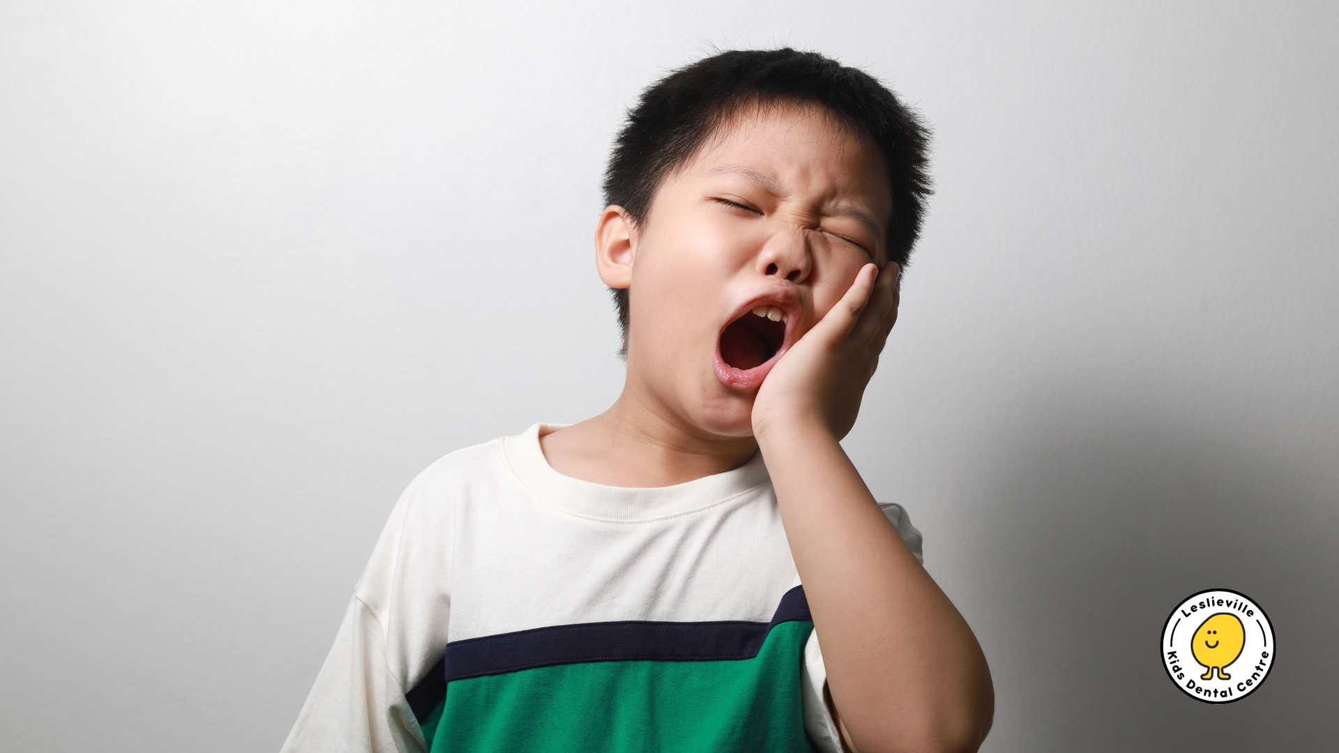 A young boy is yawning while holding his hand to his face.