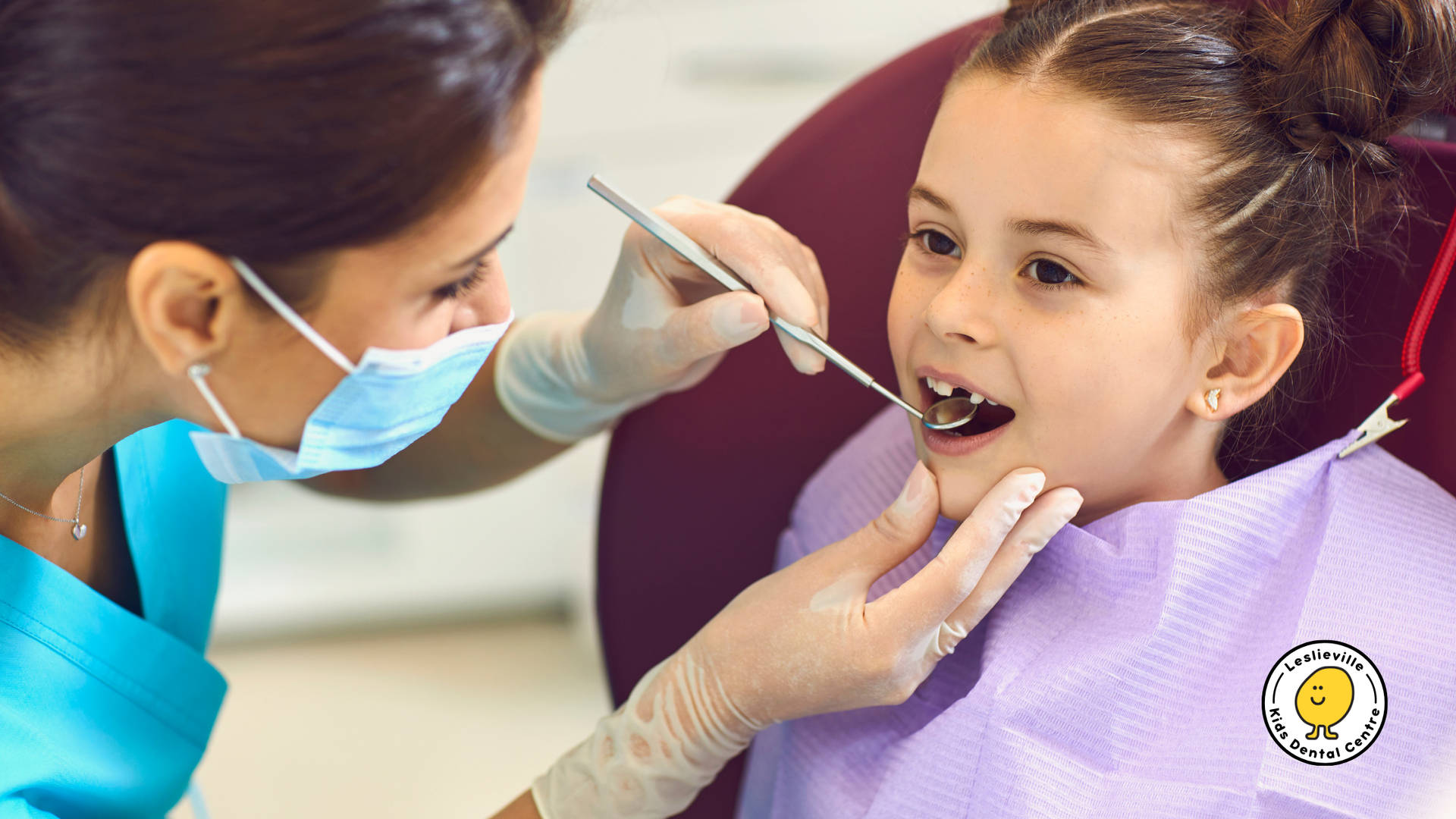 Dentist examining a young girl's teeth in a dental chair. The dentist wears a mask and gloves, while the girl has an open mouth.