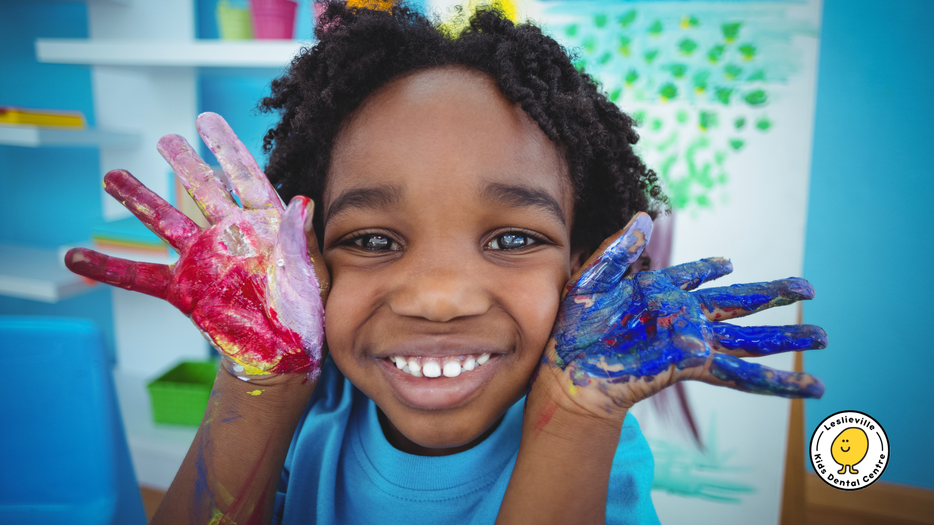 A young boy with his hands painted in different colors is smiling.