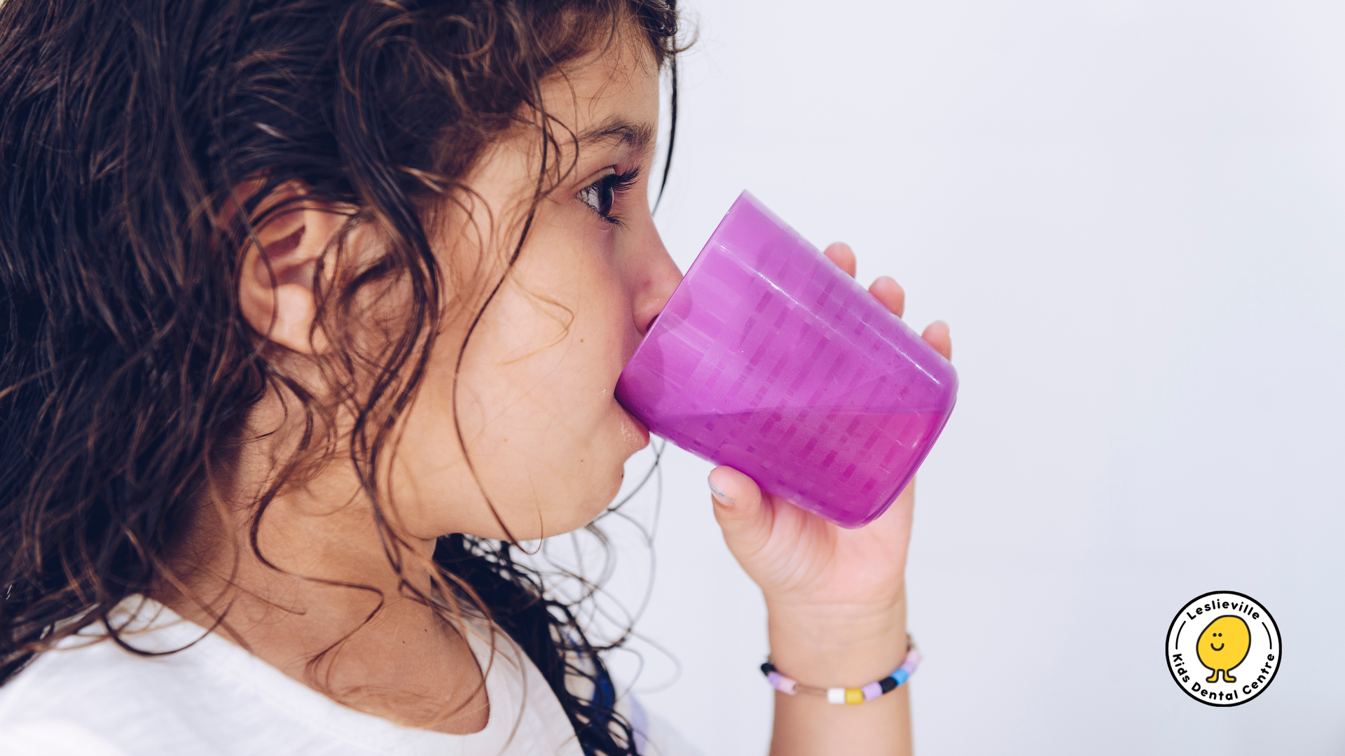 Girl with wet hair drinking from a purple cup, white background.
