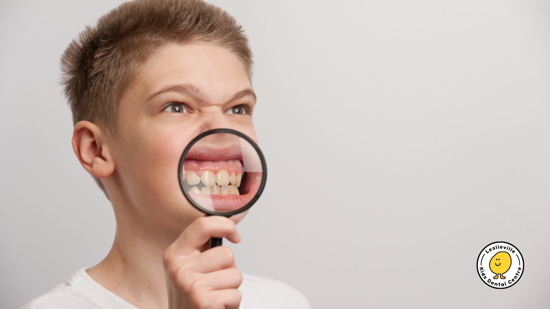 Boy holding magnifying glass over his teeth; focused, examining.