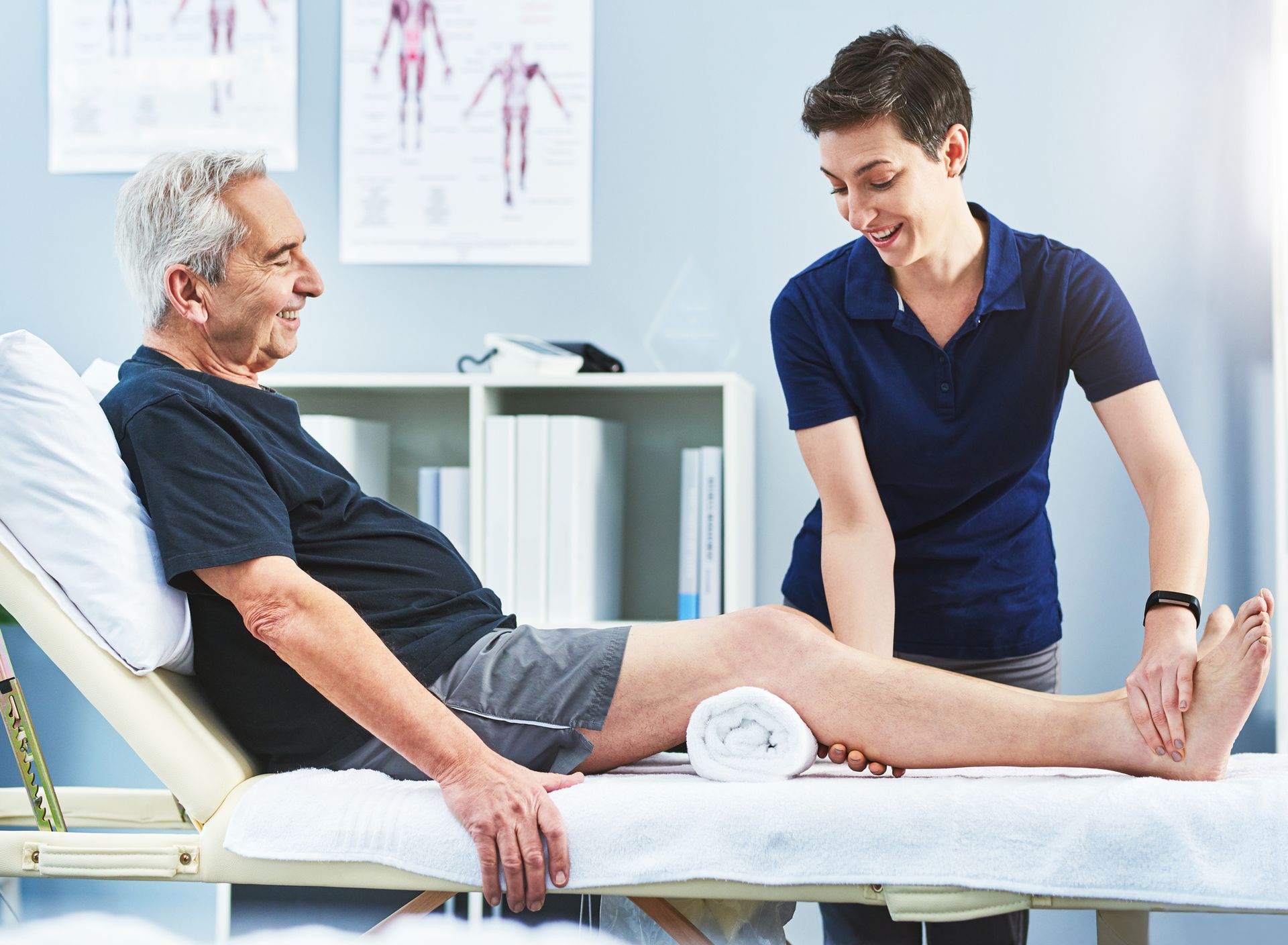 A woman is helping an older man stretch his leg.