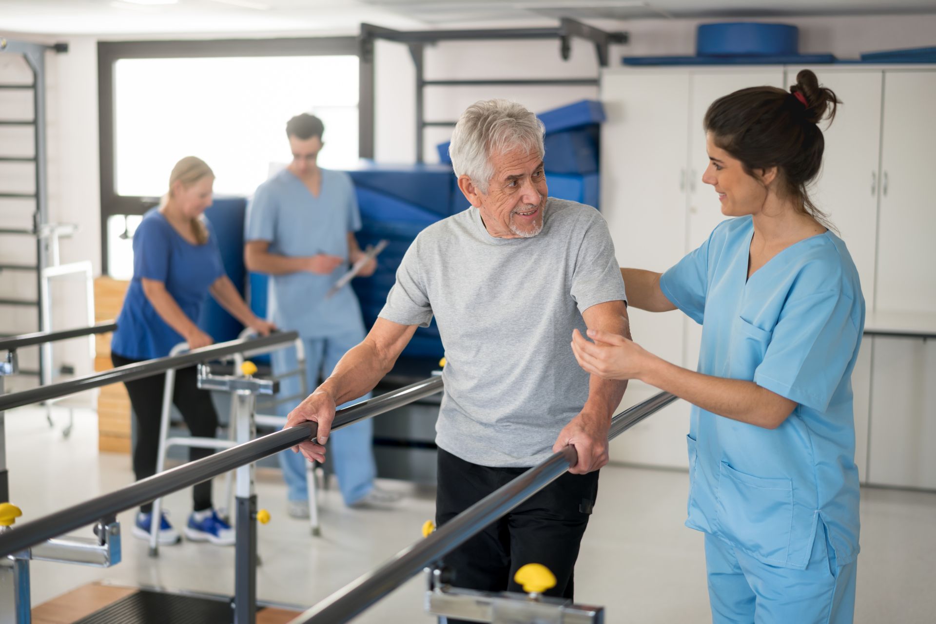 A nurse is helping an elderly man walk on parallel bars in a hospital.