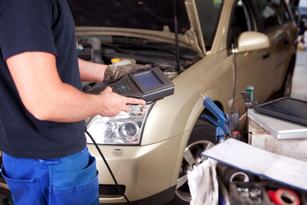 Mechanic using diagnostic tool on a gold car with the hood open in a garage  | AJM Automotive Services LLC