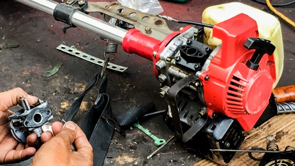 String trimmer engine being repaired on a workbench; red engine and carburetor  | AJM Automotive Services LLC