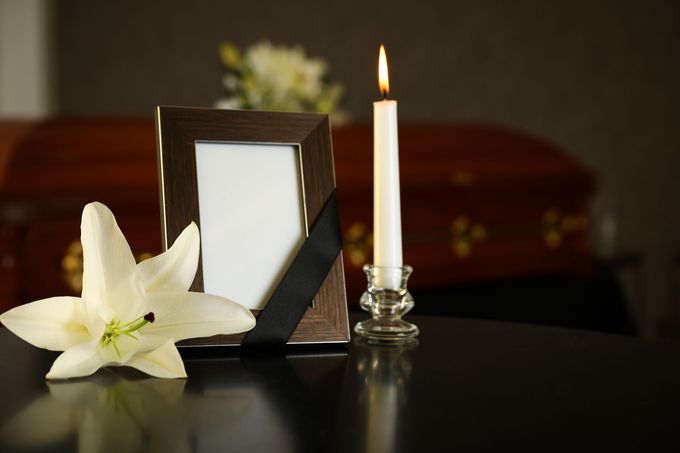 Un fiore bianco, una candela accesa e una cornice nera vuota su un tavolo scuro, a suggerire una scena commemorativa.