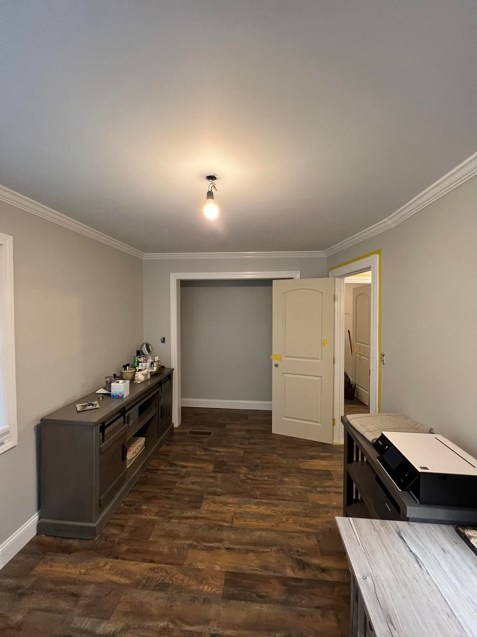 A living room with a wooden floor , a dresser , and a printer.