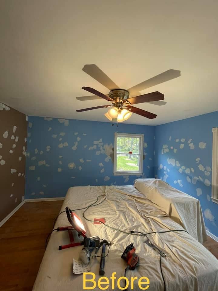 A bedroom with blue walls and a ceiling fan before being painted.