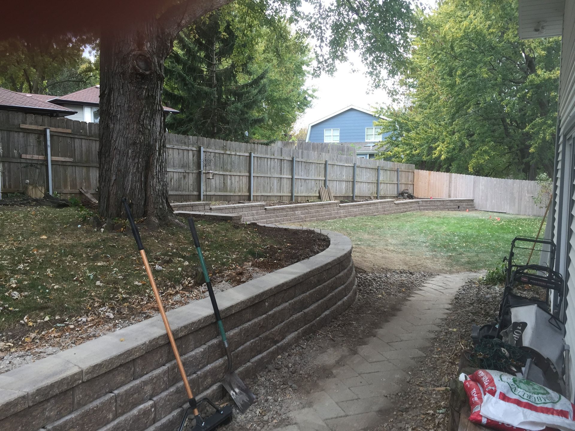 A rake and shovel are sitting on a sidewalk in front of a house.