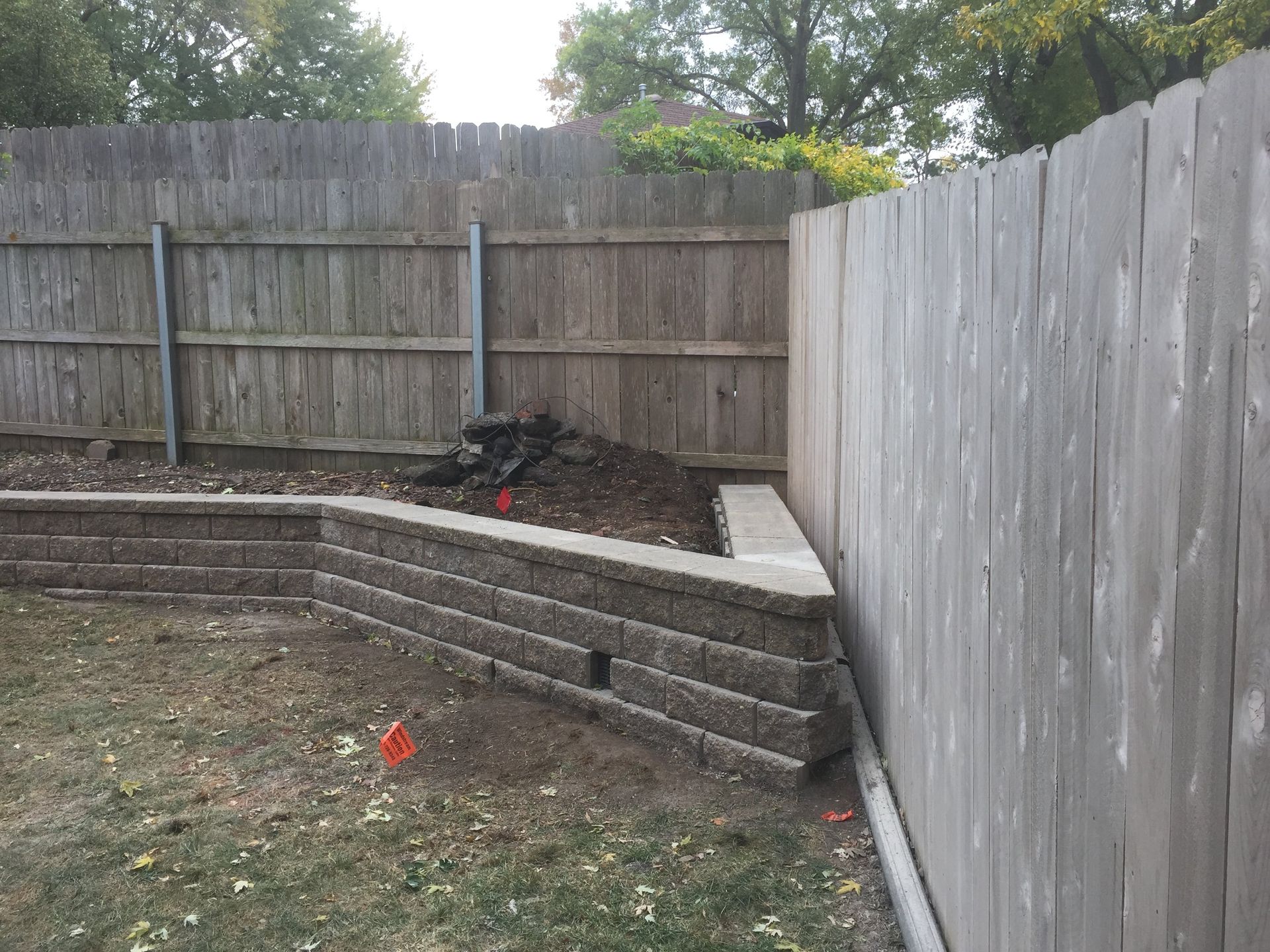 A wooden fence surrounds a brick wall in a backyard.