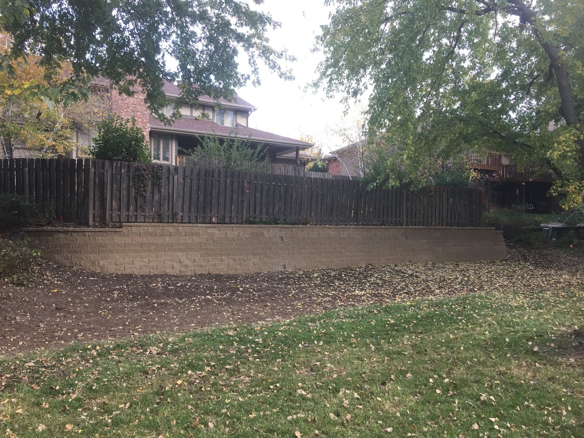 A backyard with a wooden fence and a concrete wall.