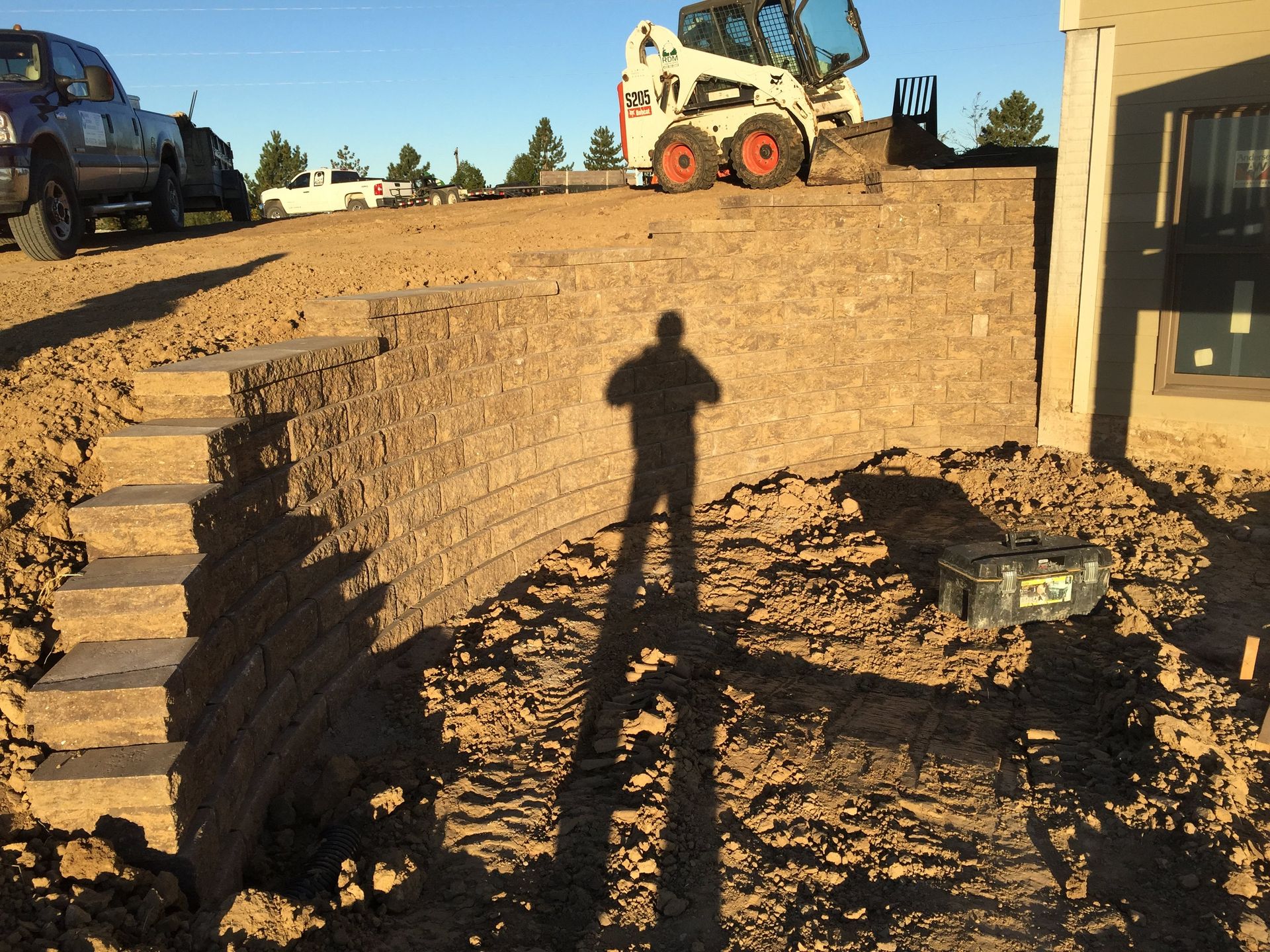 A shadow of a man is cast on a brick wall with a bobcat in the background