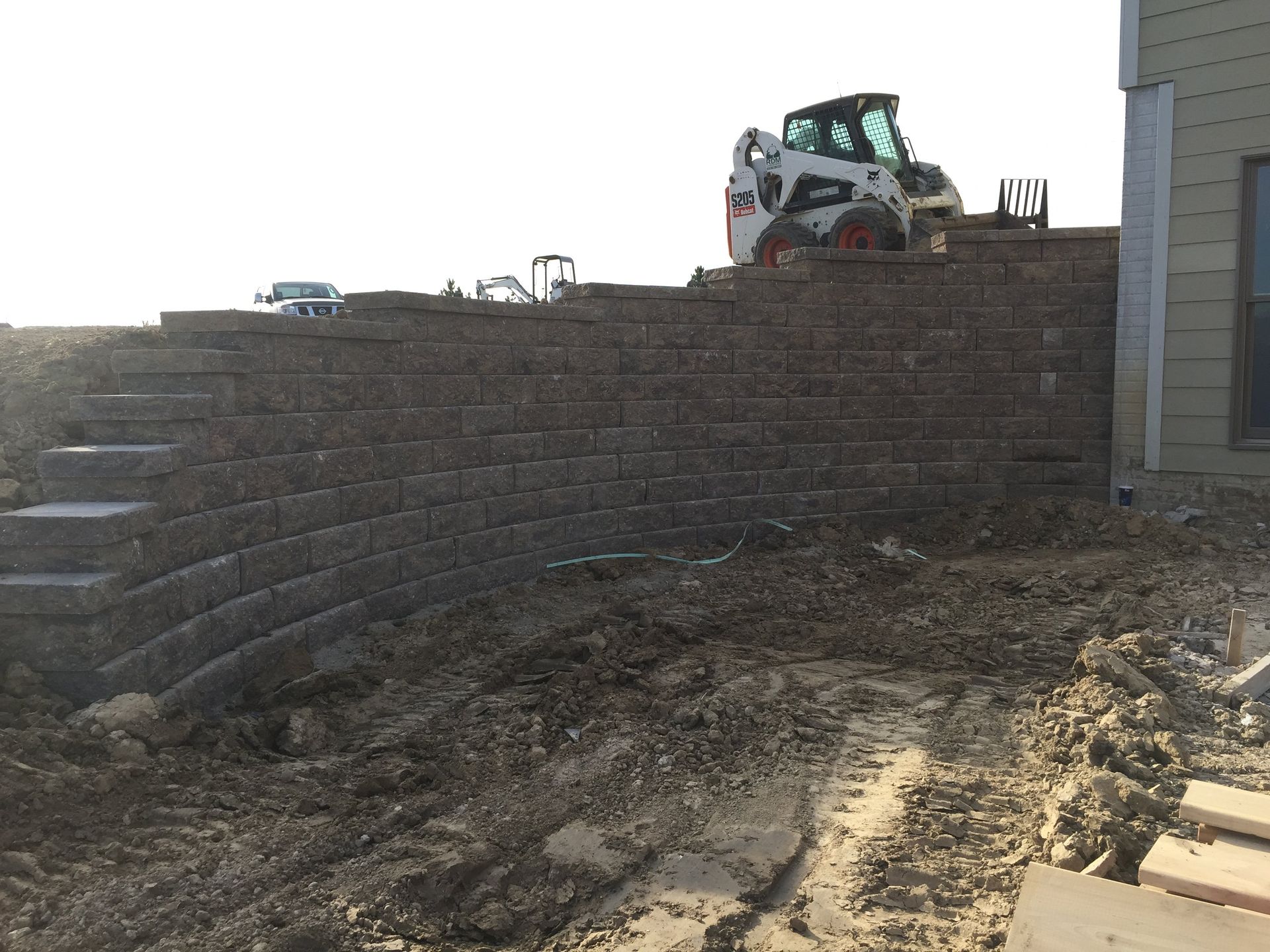 A bobcat is sitting on top of a brick wall next to a house.