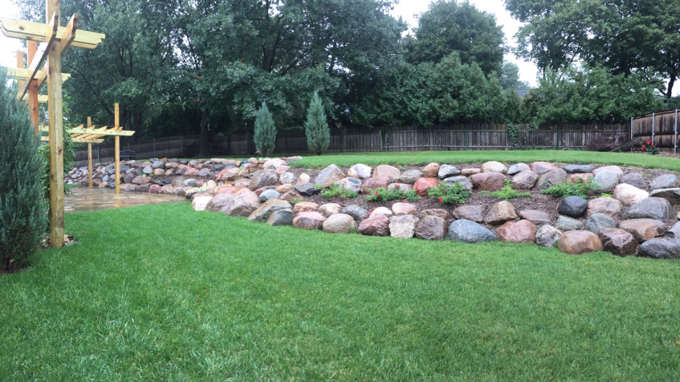 A lush green lawn with a rock wall in the background.