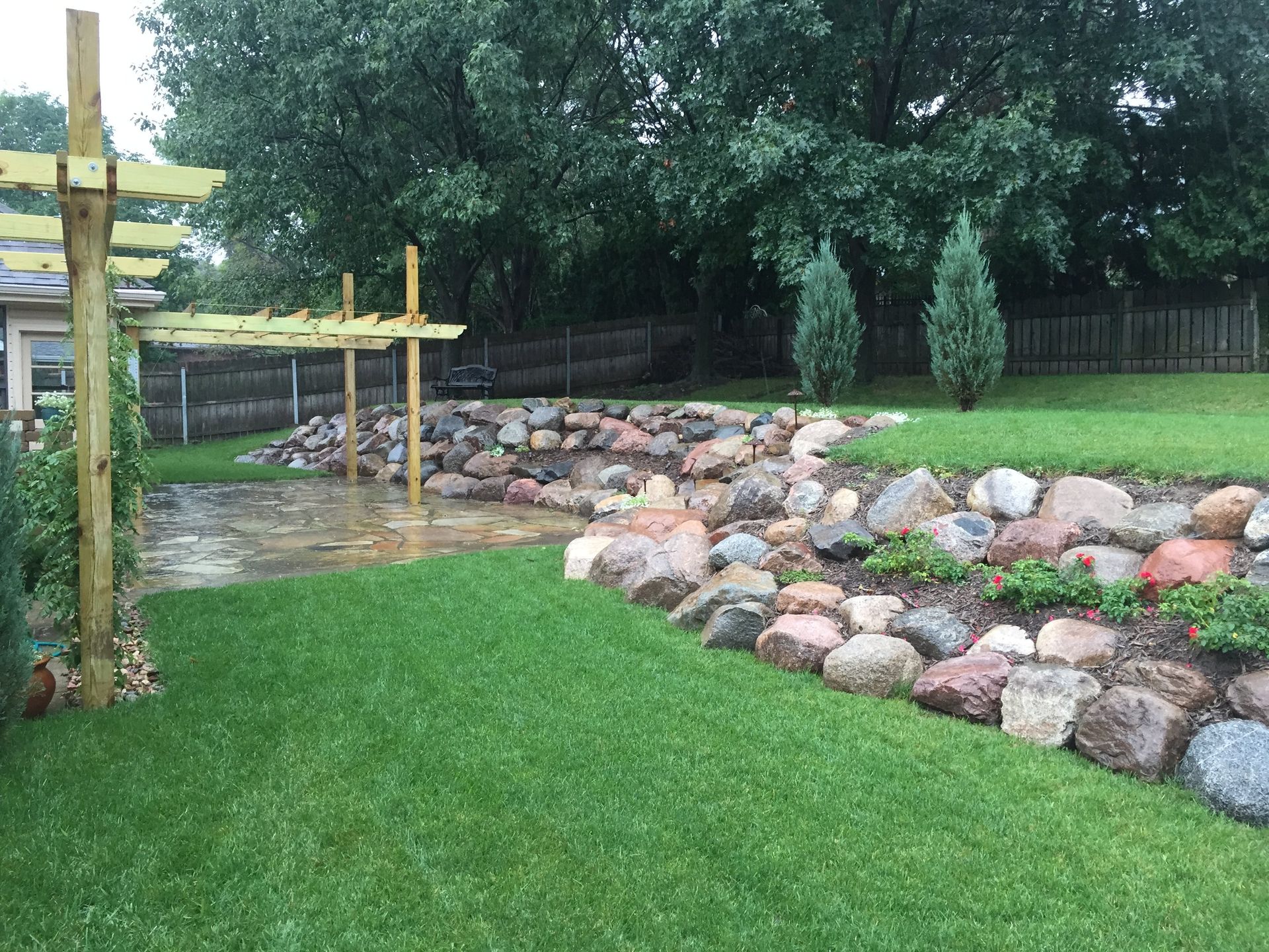 A lush green lawn with a wooden pergola and rocks in the backyard.