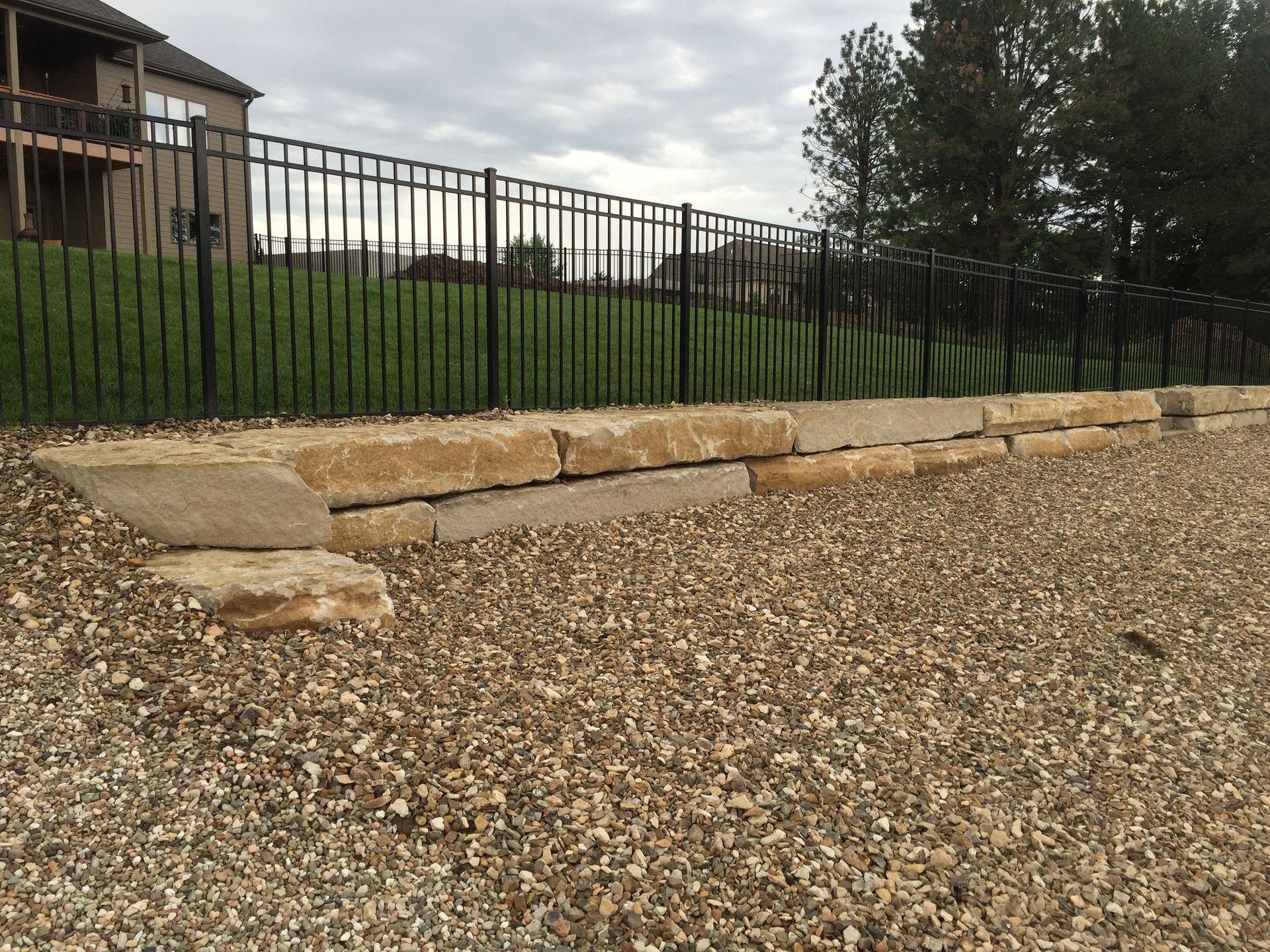 A gravel driveway with a stone wall and a metal fence.