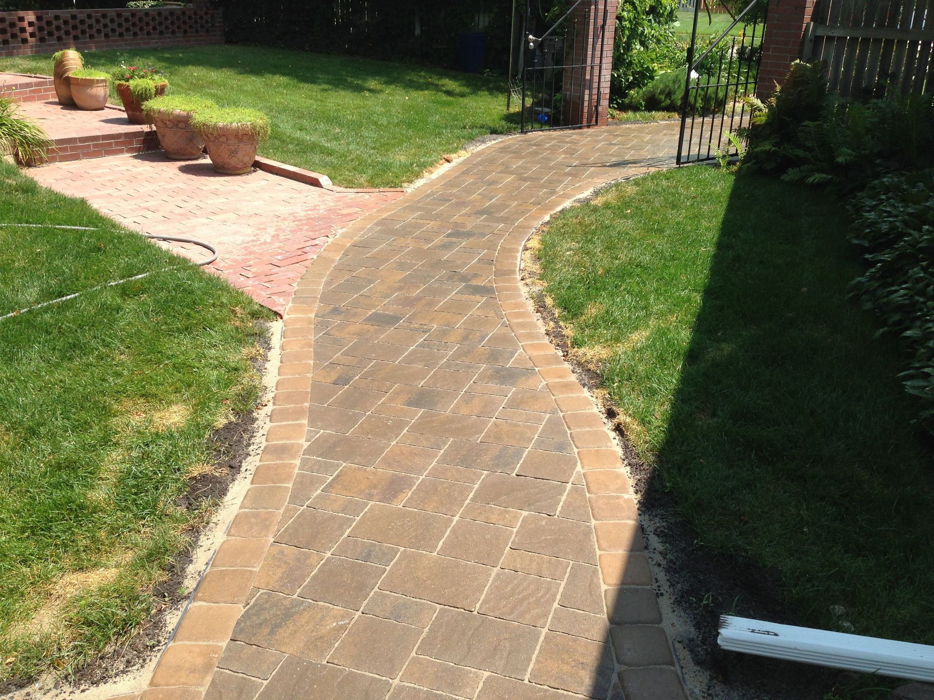 A brick walkway going through a lush green yard.