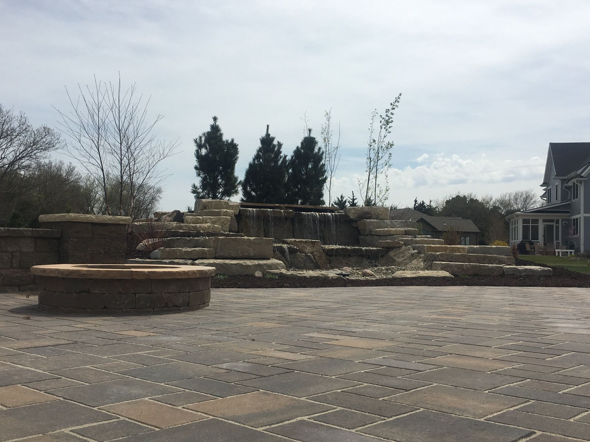 A brick patio with a fountain and trees in the background