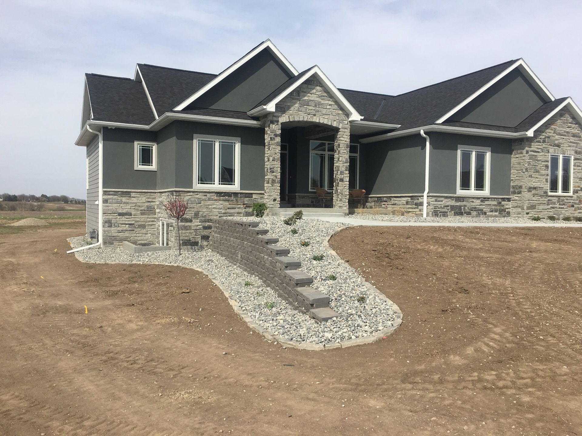 A large house with stairs leading up to it is sitting on top of a dirt field.