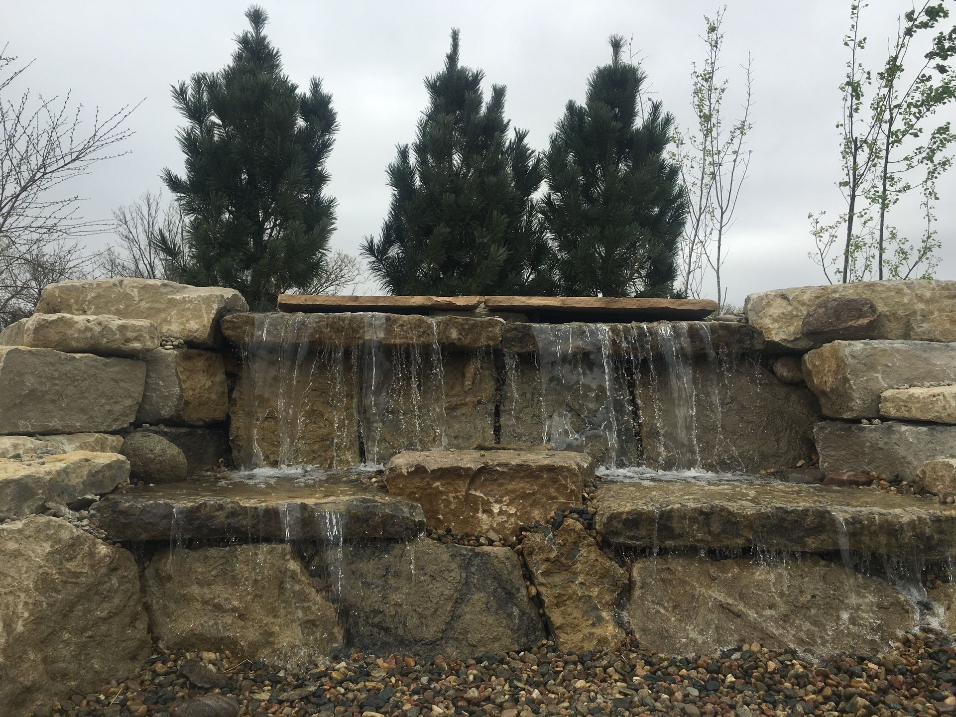 A waterfall is surrounded by rocks and gravel in a park.