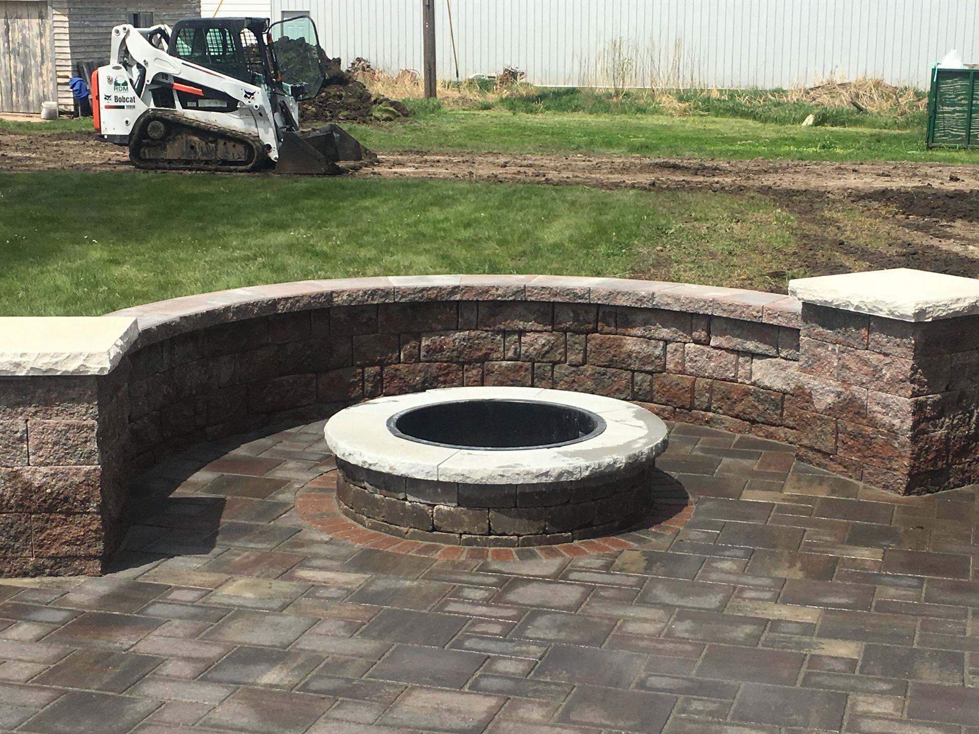 A fire pit is being built on a patio with a bulldozer in the background.