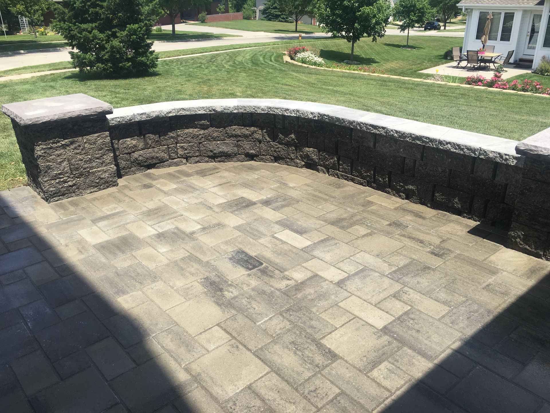 A brick patio with a stone wall and a bench in front of a house.
