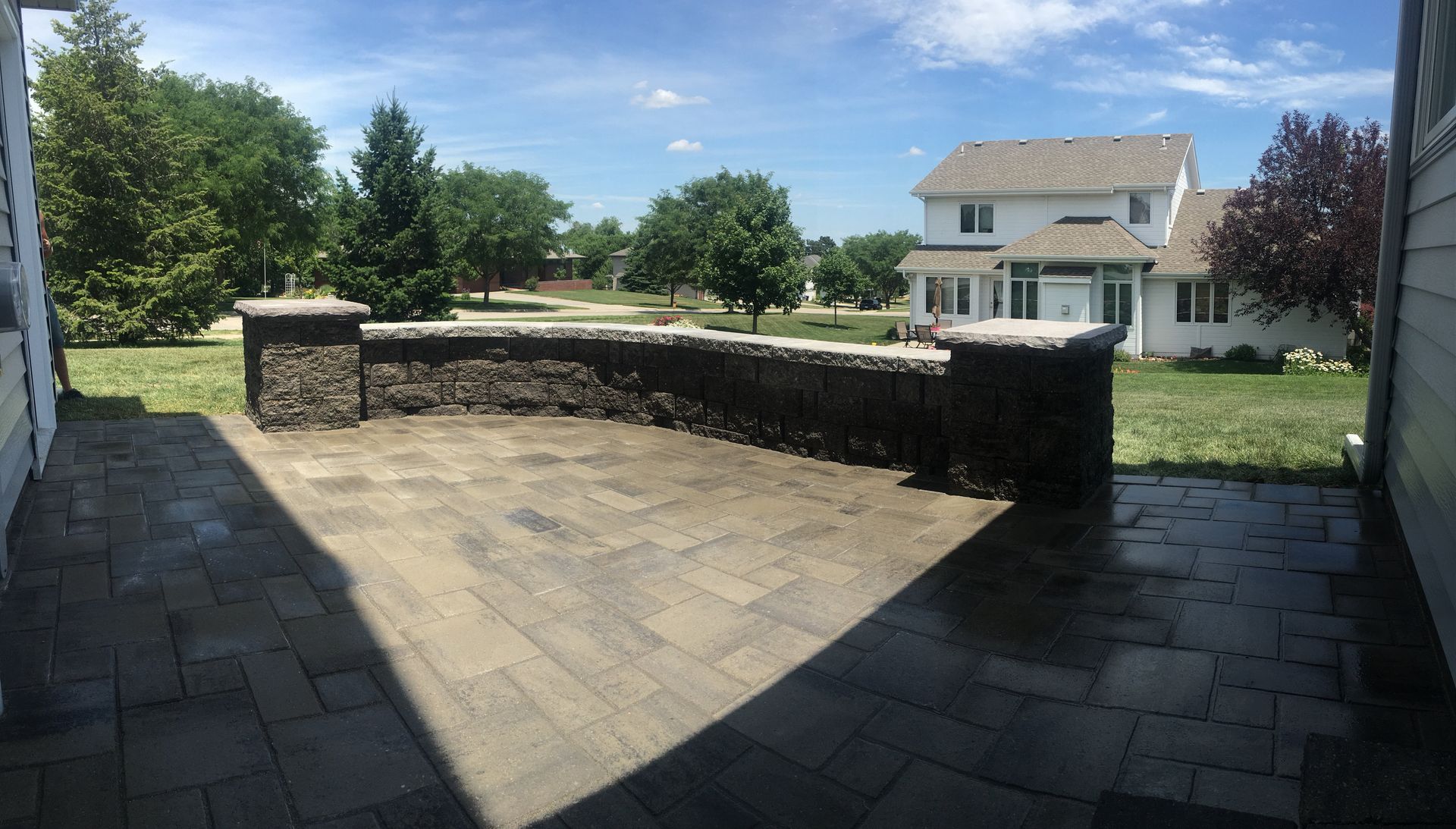 A patio with a stone wall and a house in the background