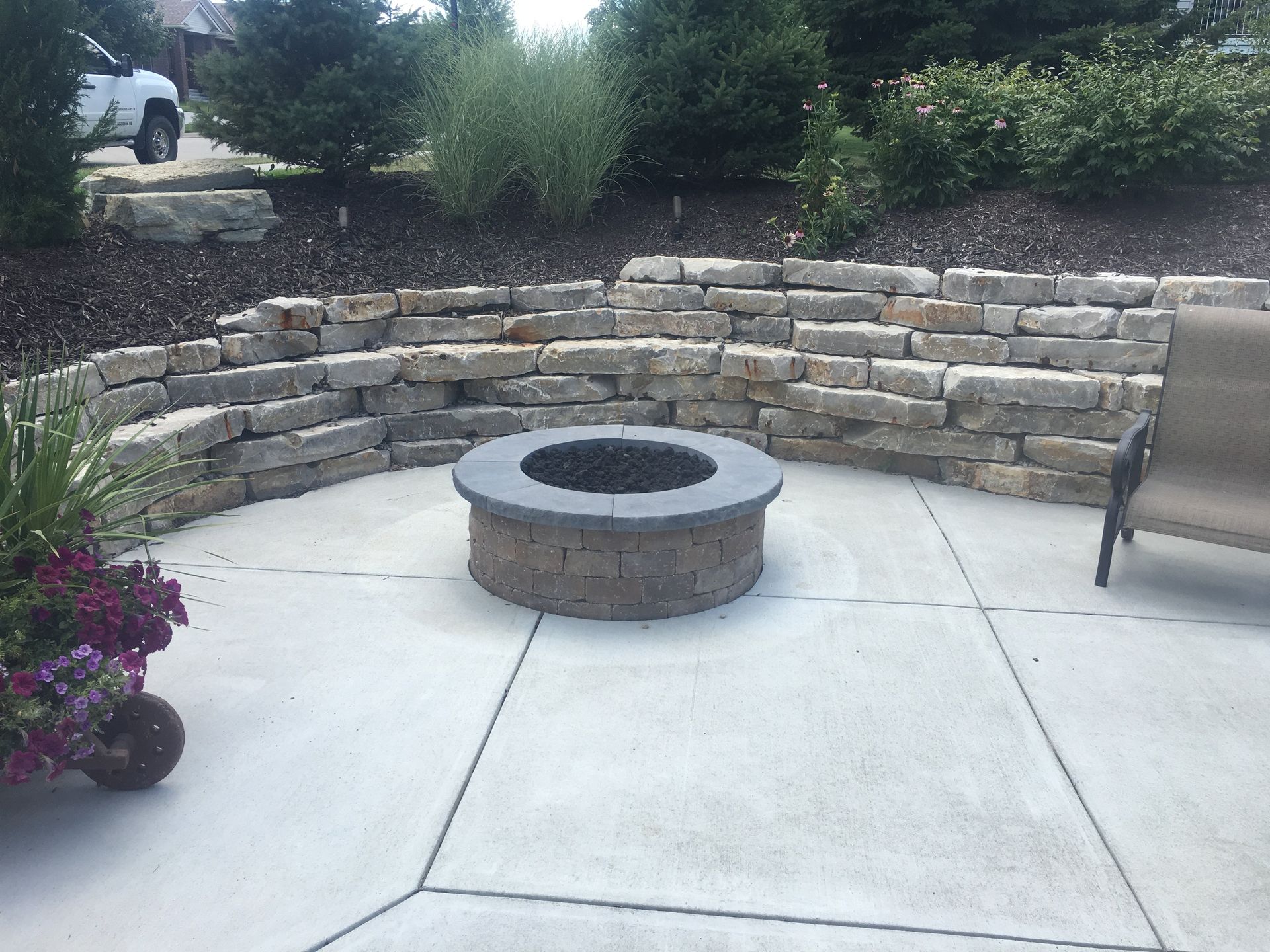 A fire pit is sitting on a patio next to a stone wall.