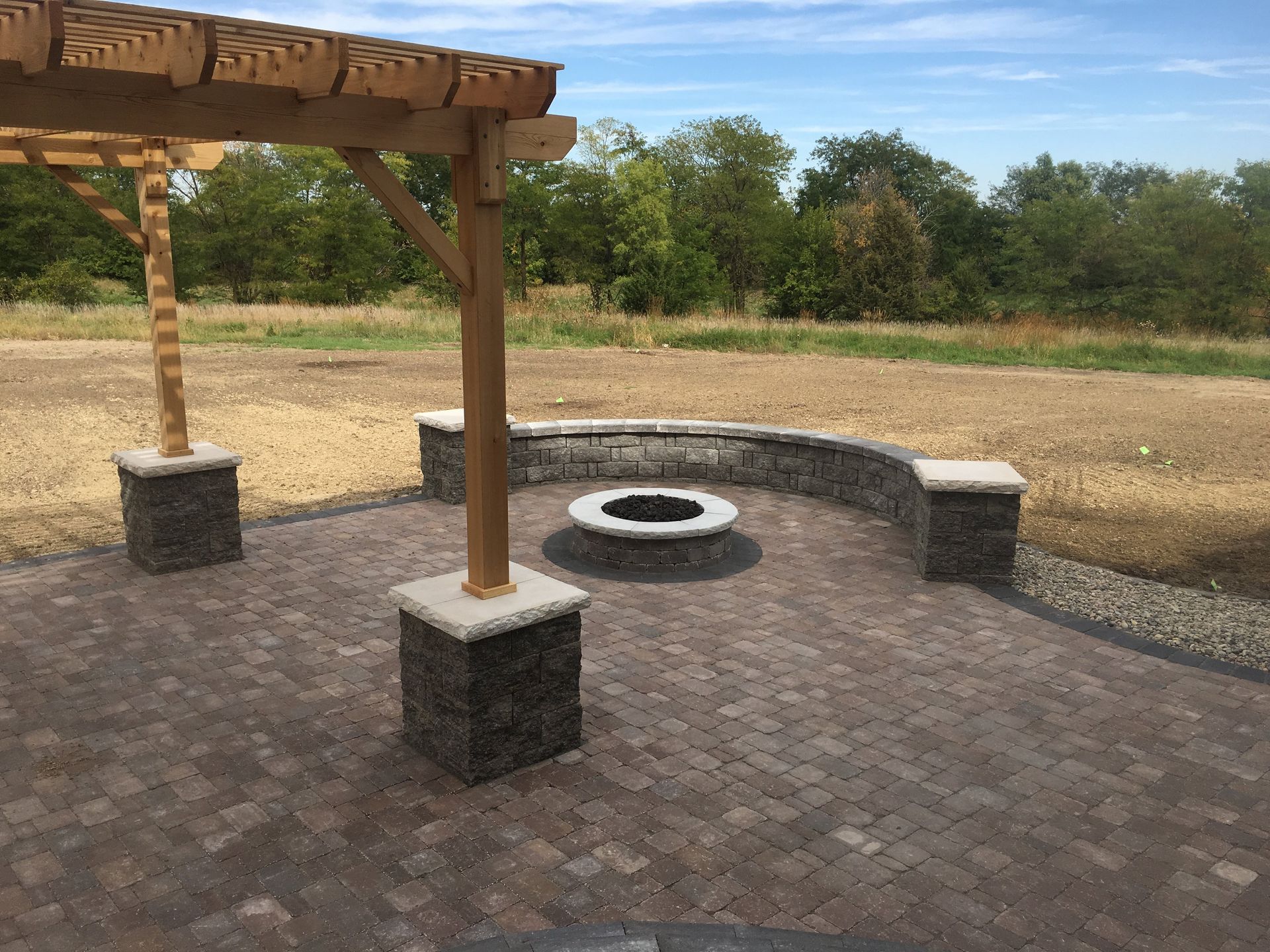 There is a fire pit in the middle of the patio under a pergola.
