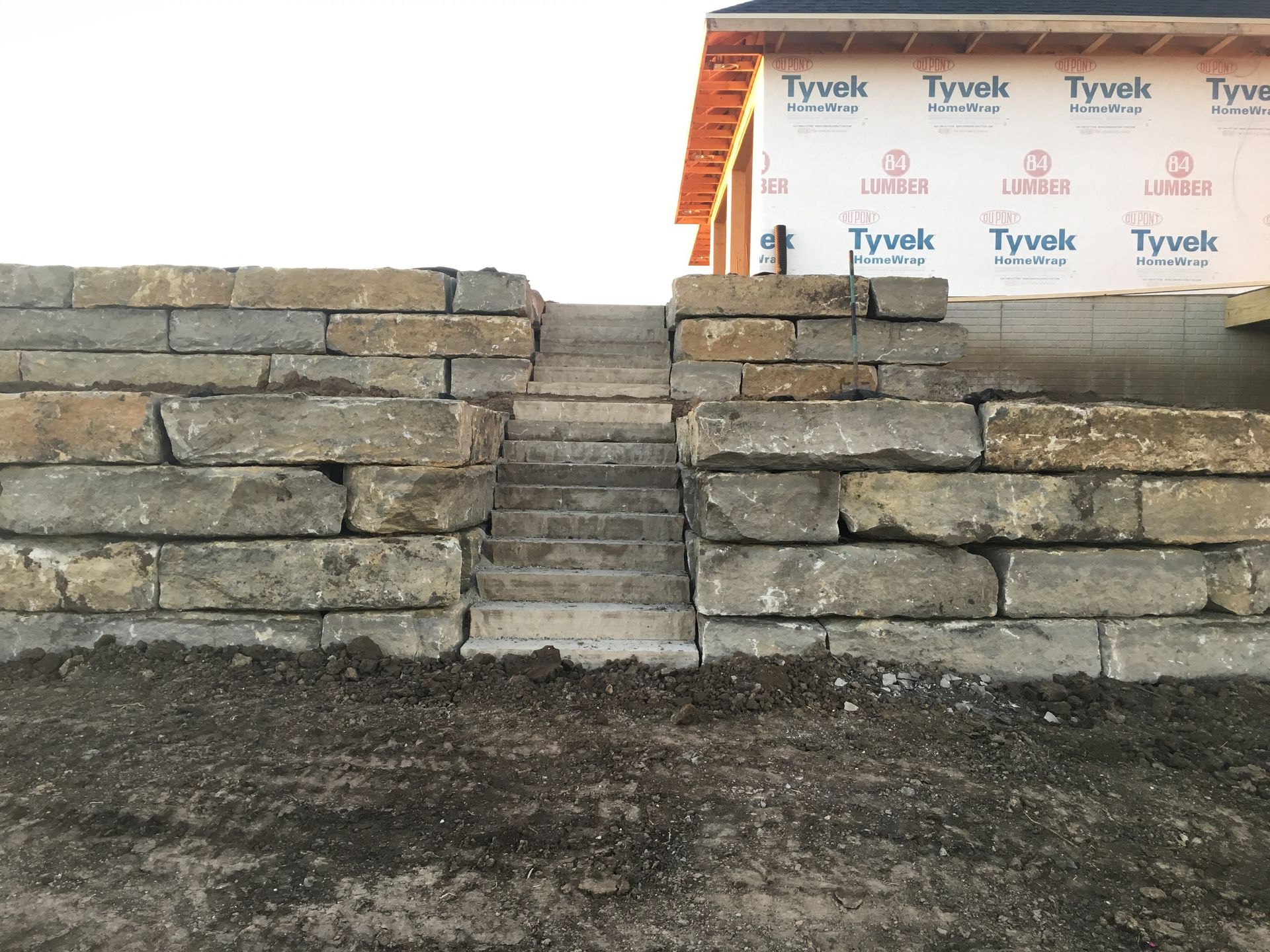 A stone wall with stairs leading up to a house under construction.