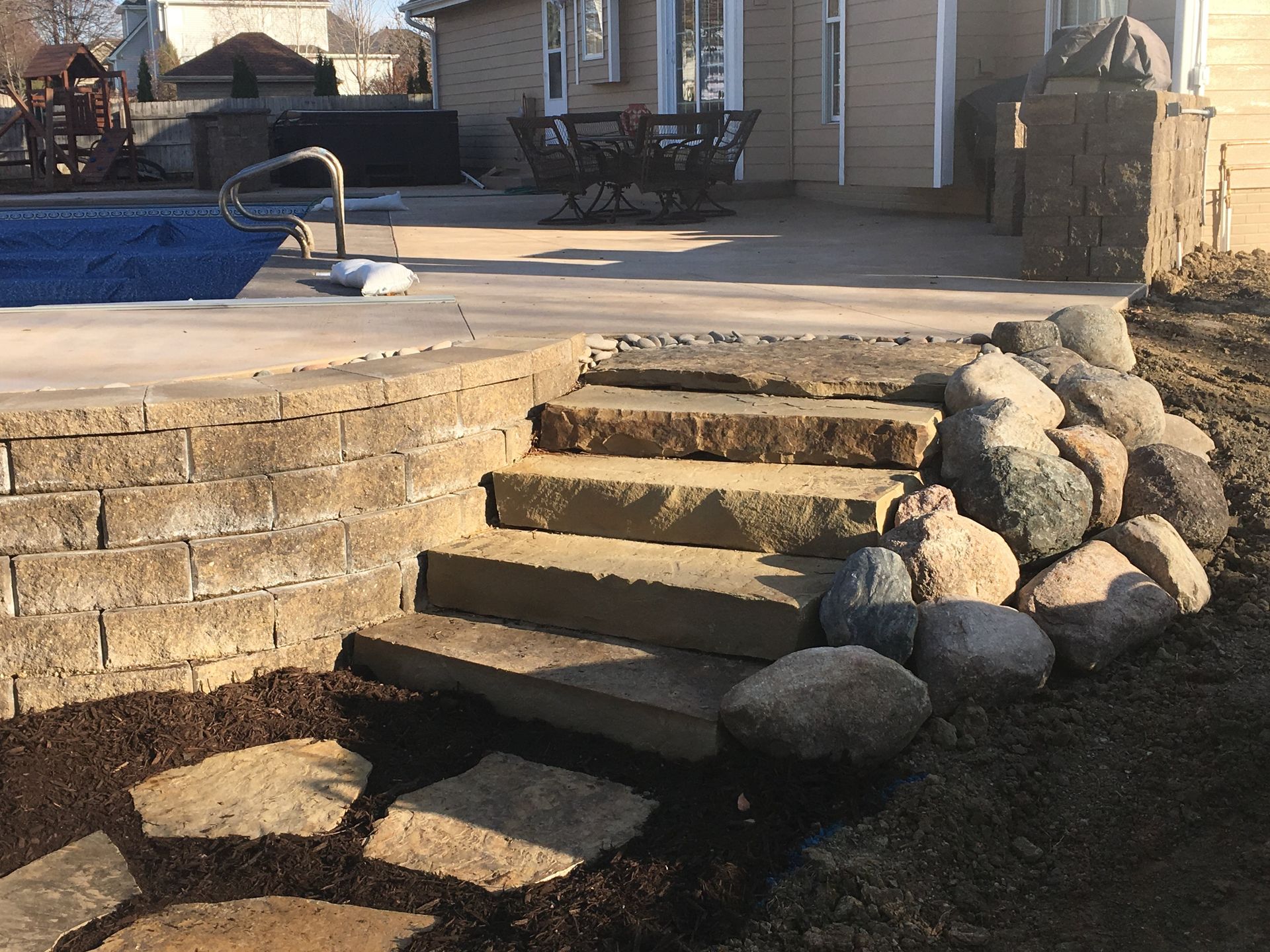 A patio with stairs leading to a pool and a house in the background.
