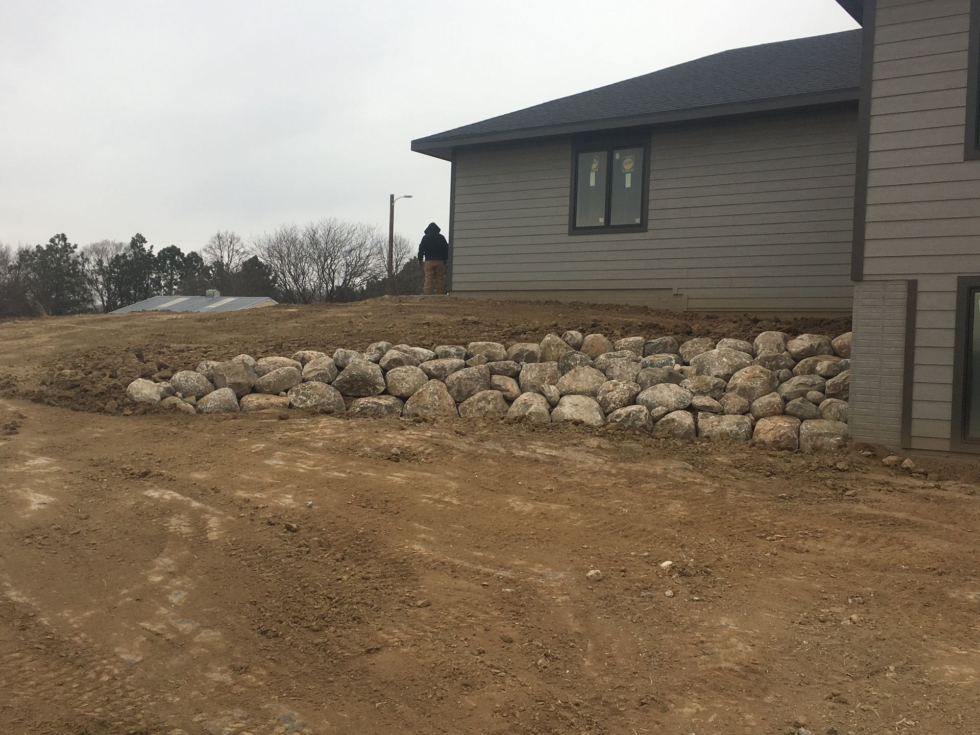 A house is sitting on top of a dirt hill next to a rock wall.