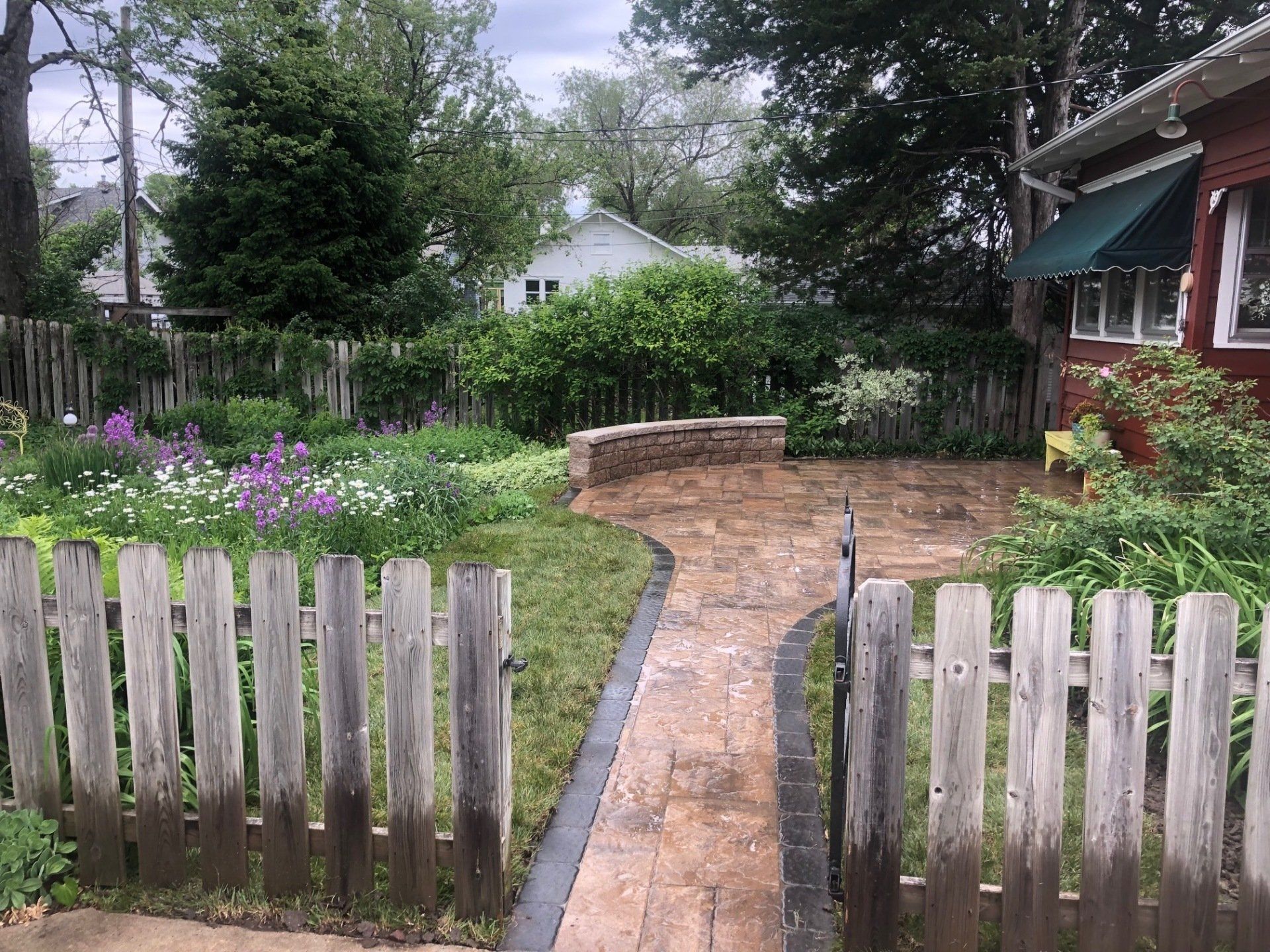 A wooden fence surrounds a brick walkway leading to a house.