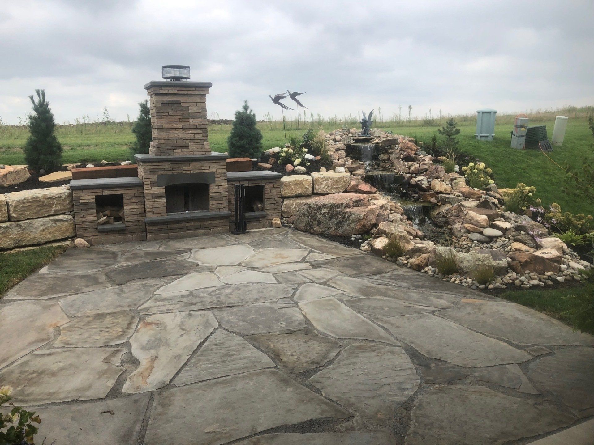 A patio with a fireplace and a waterfall in the background.